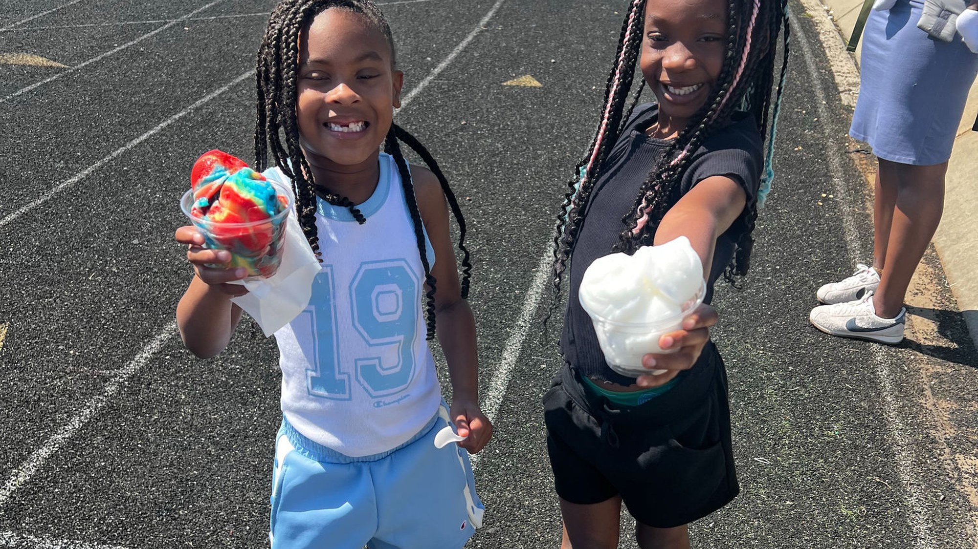 Two happy kids holding up cups of bright rainbow Italian ice at a Charlotte community event